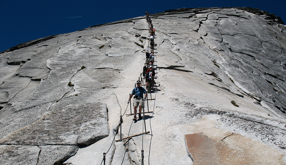 Канатная лестница на вершину Халф Дом, США
Знаете, что лежит между вами и самым известной горной вершиной Национального парка Йосемити в Калифорнии? 10-километровый путь сквозь дикую местность с постоянно возрастающим уклоном, увенчанный подъемом более чем на 100 метров вверх прямо по поверхности горы по канатной лестнице. Пройтись по ней в день могут не более 300 человек, каждому из которых дается специальное разрешение.