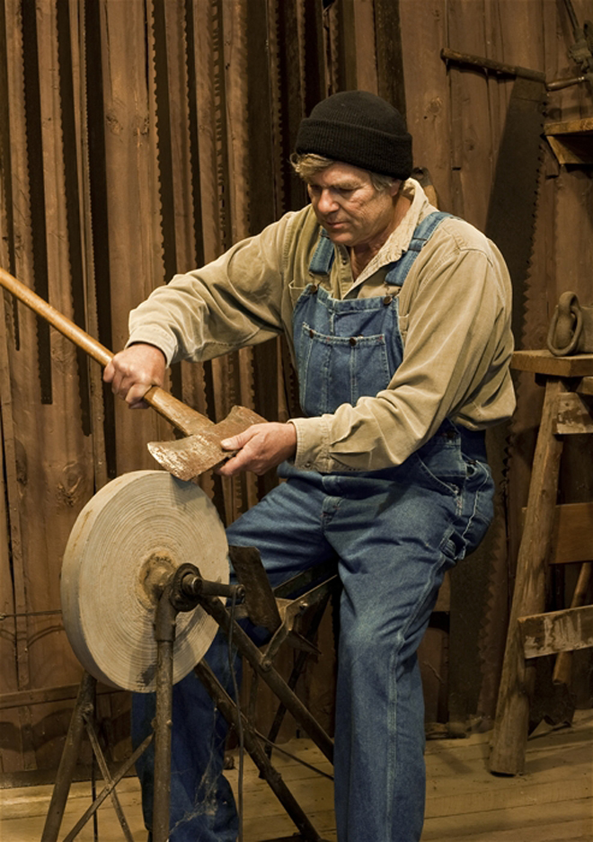 man sharpening an axe on an old pedal powered grinding stone